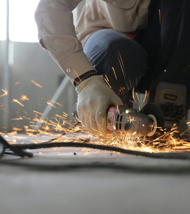 A skilled industrial worker uses a grinder creating a burst of sparks indoors.